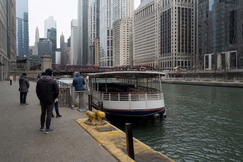 A crowded river cruise boat passing the Wrigley Building and Tribune Tower on the main branch of the Chicago River, no text, no logos, no people.
