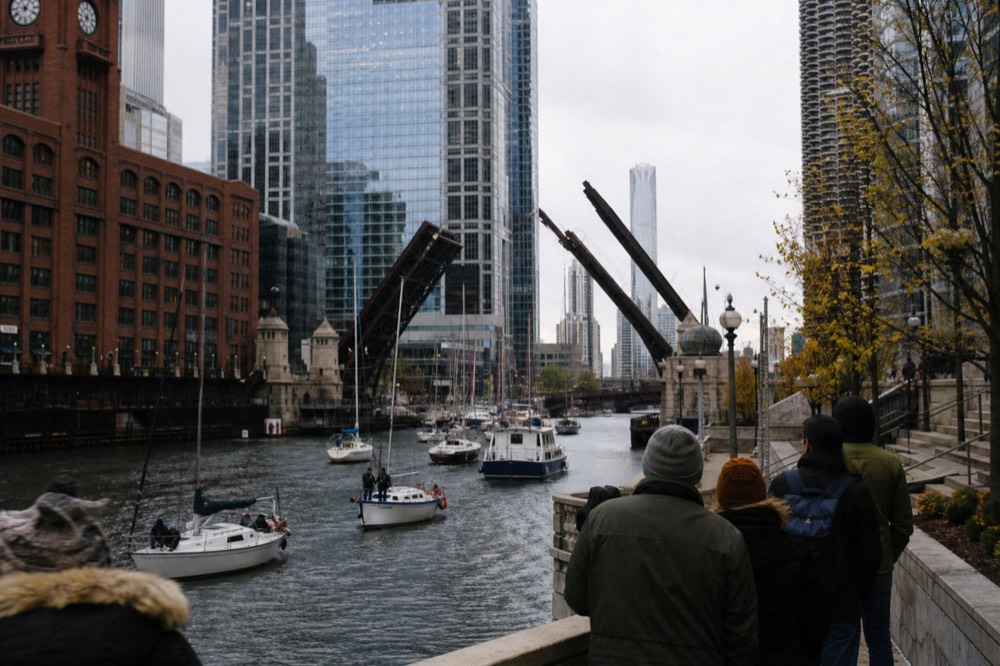 Sailboats passing through a raised bascule bridge on the Chicago River with downtown buildings behind, no text, no logos, no people.