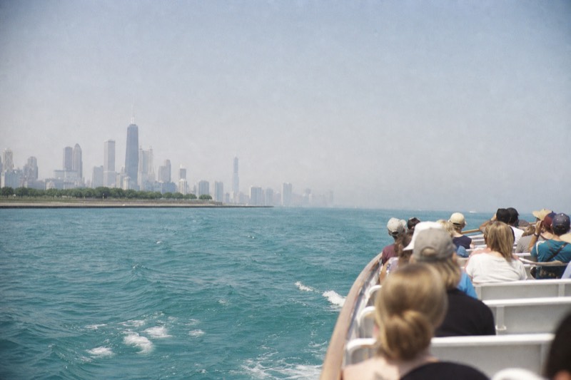 A tour boat just past the river mouth breakwater with open Lake Michigan water ahead and the skyline receding behind it