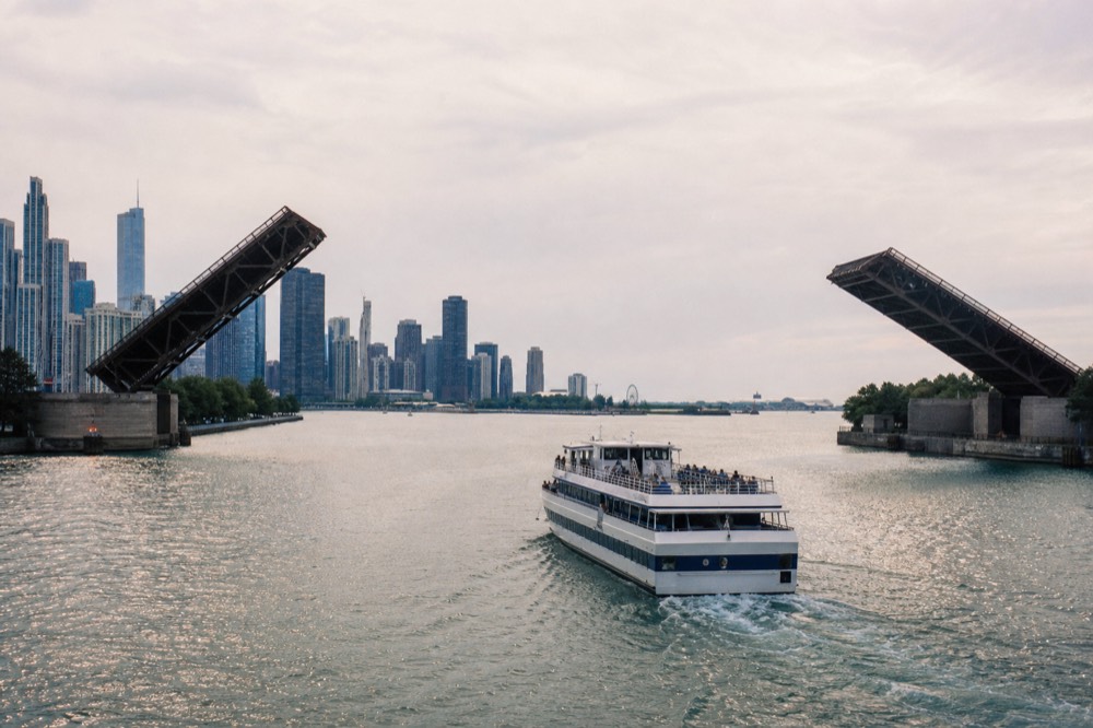 A cruise boat passing under a bascule bridge with skyline towers behind, no text, no logos, no people