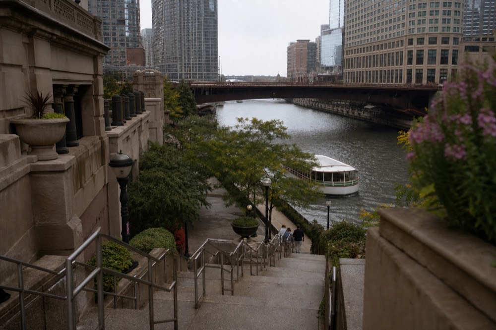 Stairs descending from a downtown Chicago street down to the Riverwalk beside the river, no text, no logos, no people