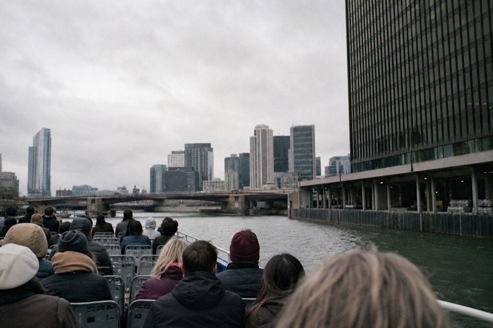 Passengers in jackets and sunglasses on an open boat deck passing under a Chicago bascule bridge, no text, no logos, no people